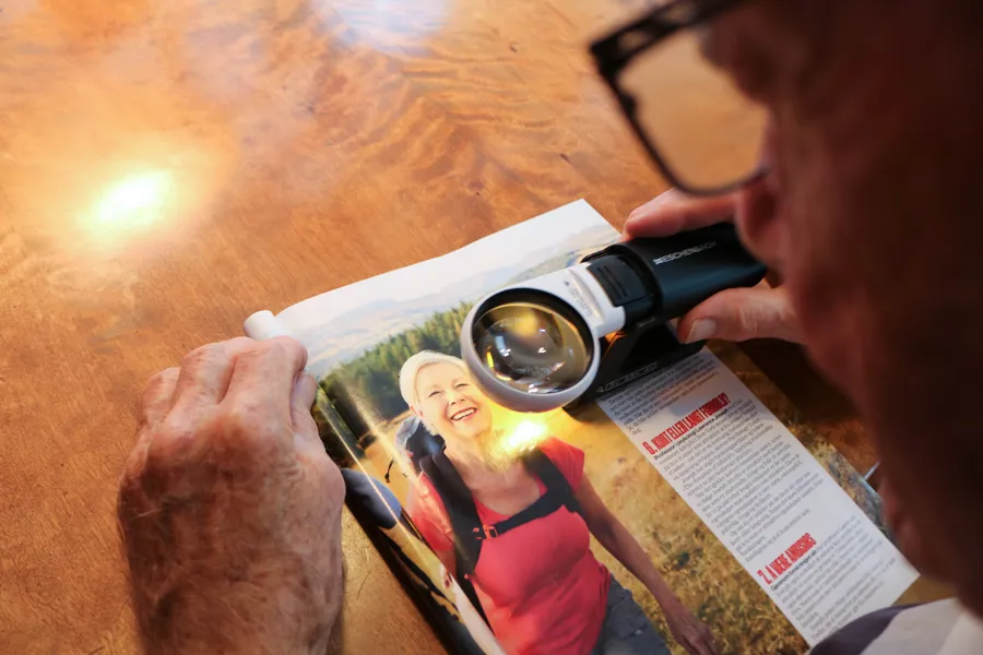 En eldre dame bruker lupe for å lese et magasin.