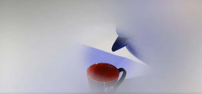 Bilde av bord, kaffekopp og noen som heller kaffe koppen. Bildet er bare skarpt på midten.