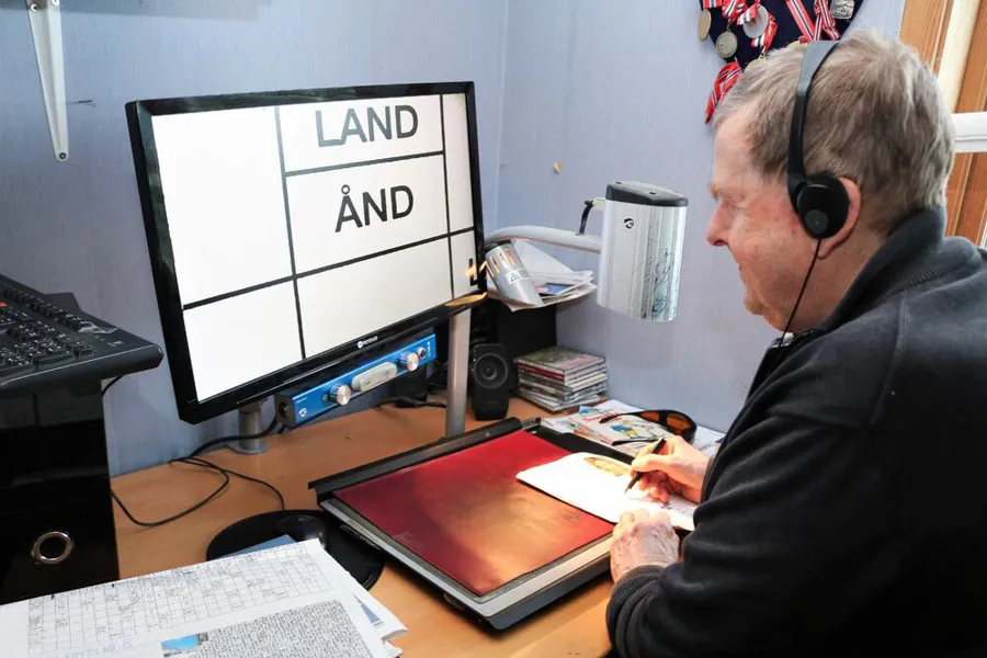 En mann med hodetelefoner og sitter ved et skrivebord med en lese-TV.