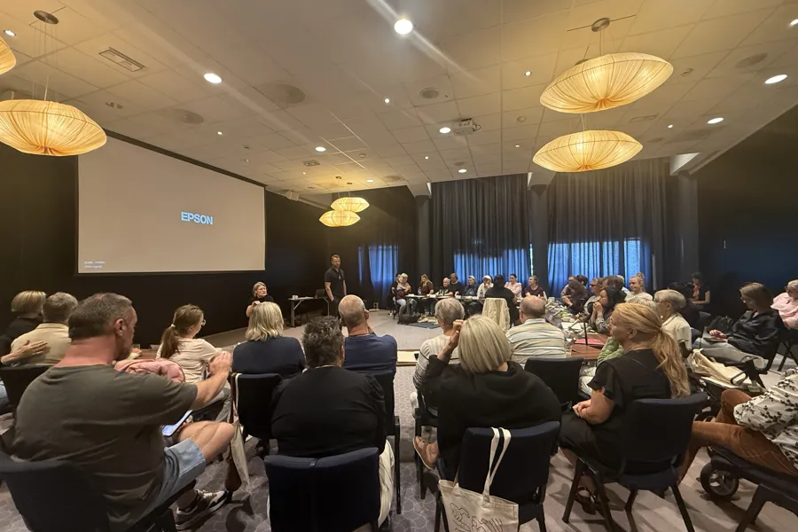 En gruppe mennesker som sitter i et rom med en scene og en person som står foran dem