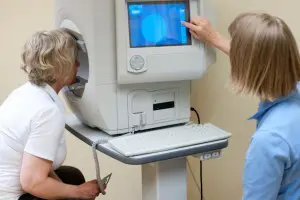 Bilde av to kvinner, der kvinnen til venstre har ansiktet inne i en maskin og kvinnen til høyre ser og trykker på en skjerm.