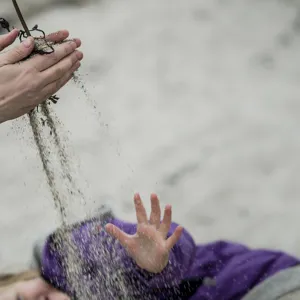 Hender som leker med sand.